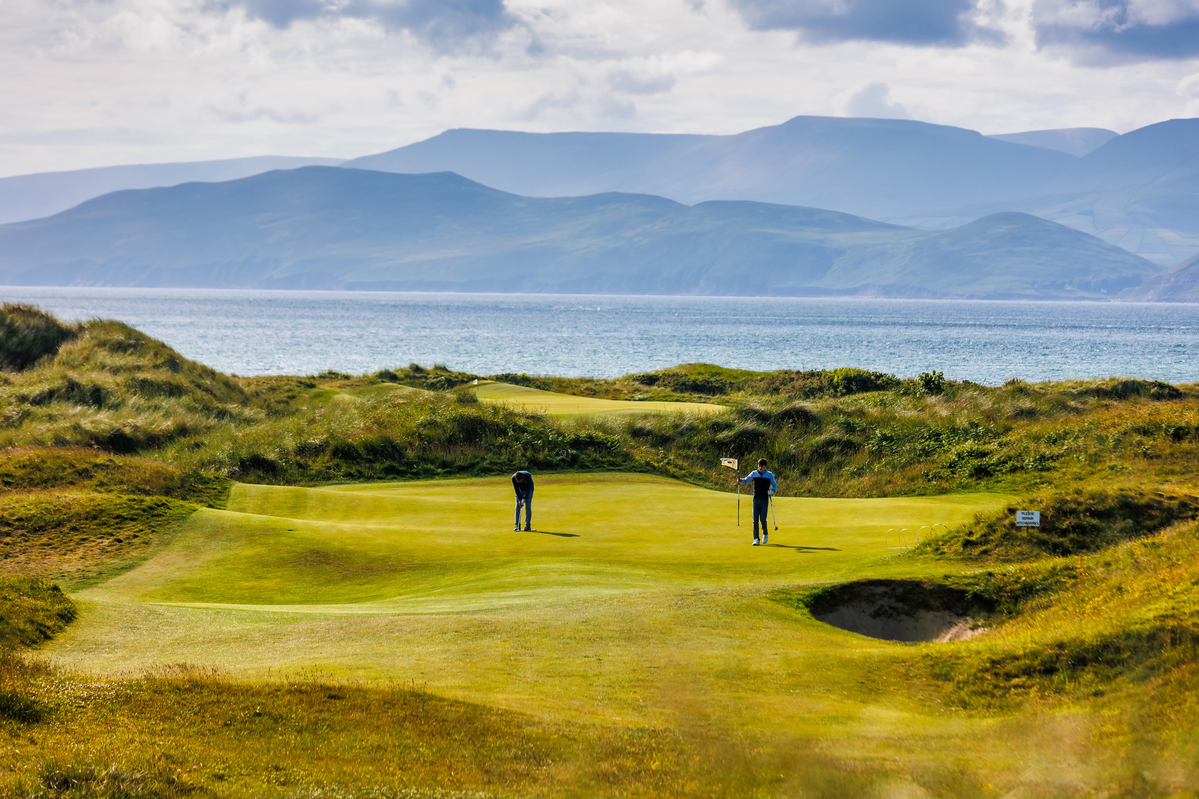 Two golfers on a Dooks green with mountains and sea beyond