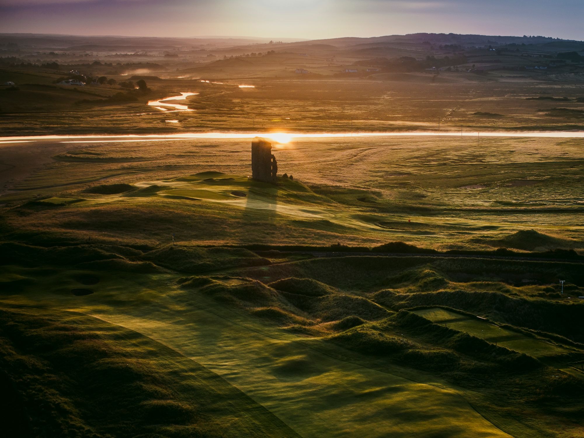 Aerial sunrise view of Lahinch Golf Club with the ruined castle tower and the Atlantic beyond